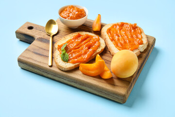 Wooden board of tasty sandwiches with apricot jam on color background