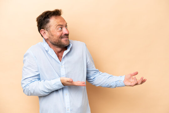 Middle age caucasian man isolated on beige background with surprise expression while looking side