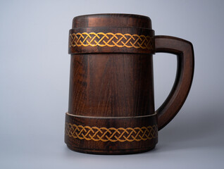 Wooden oak mug with a handle on a gray studio background. Brown mug with ornament. Handmade wooden tankard for beer or kvass. Rustic background.