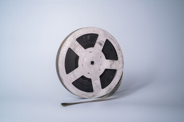 Old scratched metal reel with audio or video tape on a gray studio background. Bobbin, retro magnetic spool. Round reel for analogue projector or sound record. Videotape, filmstrip.