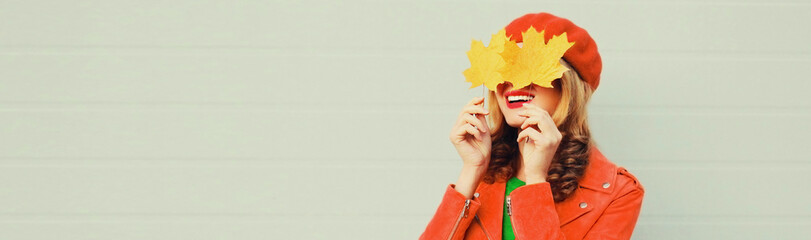 Autumn portrait close up of happy woman covering her eyes with yellow maple leaves on gray background