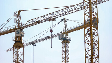 Fototapeta na wymiar Three big yellow building crane on construction site. Morning sky background.