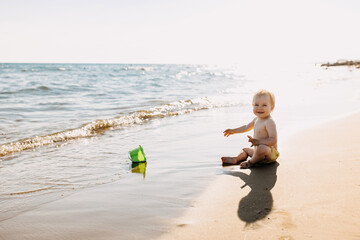 Little child sitting alone on a seashore playing with a green bucket, smiling