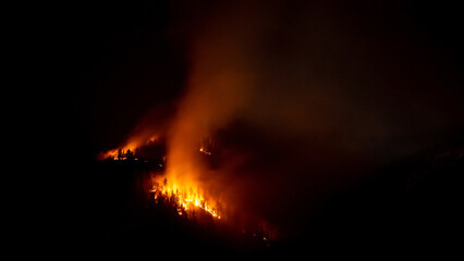 Wildfire smoldering on the mountain range, burning forest