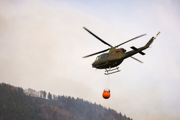 Fototapeta na wymiar Localized wildfire with the helicopter dropping water by using a water bucket attached to a long line under the helicopter