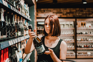 Young woman taking bottle of champagne wine from shelf at supermarket