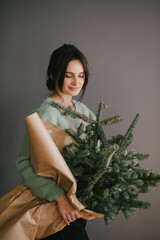 Millennial woman holding big bunch of pine branches wrapped in craft paper, going to make Christmas wreath and festive holiday decorations