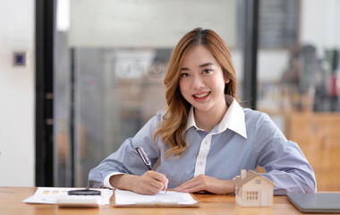 Miniature house in the hands of an Asian woman real estate agent home loan working at the office. Looking at the camera.