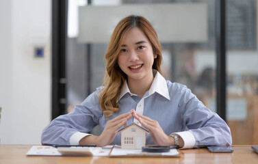 Miniature house in the hands of an Asian woman real estate agent home loan working at the office....
