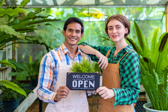 Team of diversity garden worker holding opening sign to welcome customer to their tropical nursery plant center full of exotic fern species