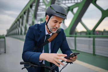 Businessman commuter on the way to work, pushing bike on bridge and texting on mobile phone,...