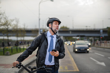 Portrait of businessman commuter on the way to work, pushing bike and using mobile phone, sustainable lifestyle concept.