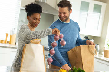 Image of happy diverse couple unpacking groceries in kitchen