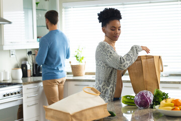 Image of happy diverse couple unpacking groceries in kitchen