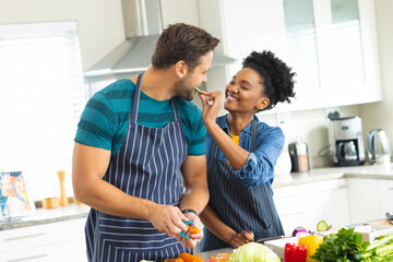 Image of happy diverse couple cutting vegetables and preparing meal together