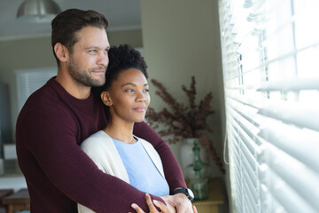 Image of diverse couple embracing and looking outside window