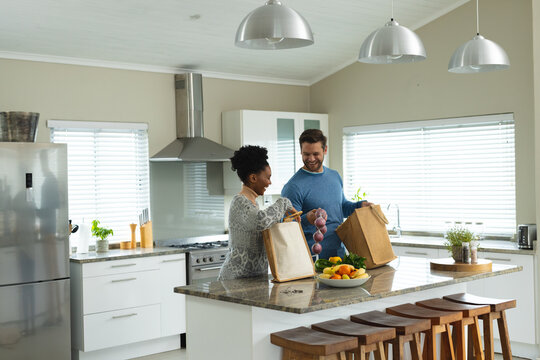 Image of happy diverse couple unpacking groceries in kitchen
