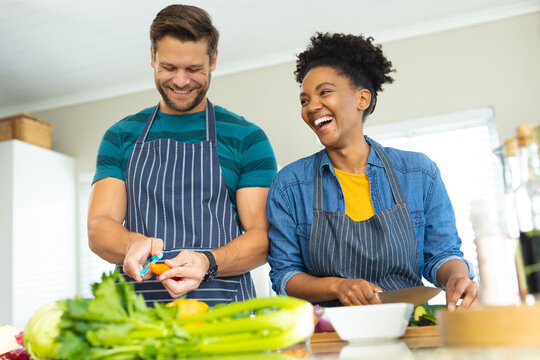 Image of happy diverse couple cutting vegetables and preparing meal together
