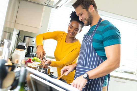 Image of happy diverse couple preparing meal together in kitchen