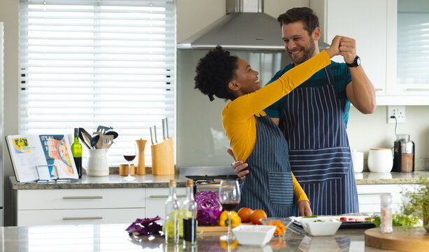Image of happy diverse couple dancing in kitchen