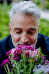 Portrait of happy mature businessman sitting outdoor and smelling flowers.