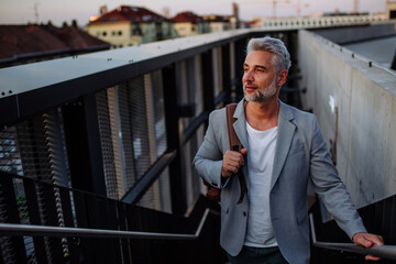 Successful happy businessman commuting in city street, looking away.