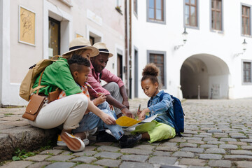 Multiracial family travel together with suitcases, sitting on ground and looking at the paper map.