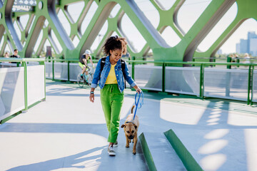 Multiracial girl walking with her dog outside in the bridge, training him, spending leisure time together. Concept of relationship between dog and teenager, everyday life with pet.