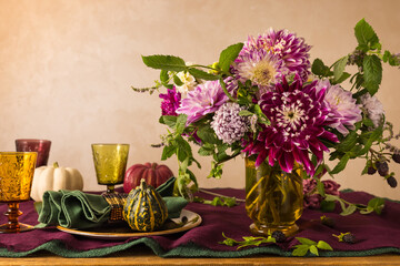 Festive table setting for Thanksgiving day. Autumnal decorations,plates, multicolor glasses and beautiful garden flowers.