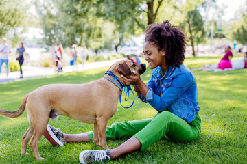 Multiracial girl sitting and resting with her dog outside in the park, training him, spending leisure time together. Concept of relationship between dog and teenager, everyday life with pet.