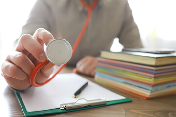 Male doctor search information in book and writtnig prescription, medical stethoscope on the desk at clinic. Medical knowledge and education concept.