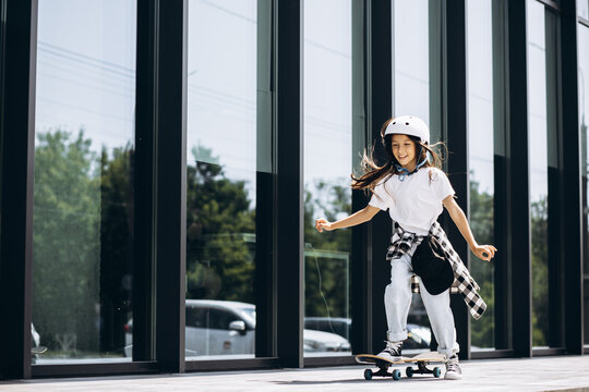 Cute school girl skating on skate board in the city wearing safety helmet
