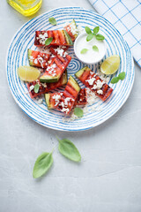 Grilled watermelon with grated cheese and white yogurt, high angle view on a light-grey stone background, vertical shot with space
