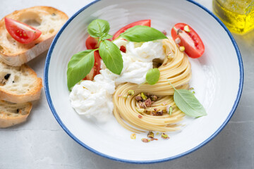 Plate of spaghetti with stracciatella or stretched curd cheese, pistachios and green basil, middle...