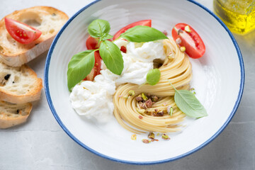 Plate of spaghetti with stracciatella or stretched curd cheese, pistachios and green basil, middle close-up, selective focus