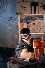 Drop shipping business owner wears white clay skull, professional makeup in home office. accepts an order on the site writes the address on the box. Festive decorated office. halloween sale