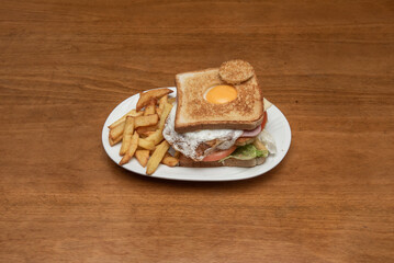 A delicious and satisfying extreme sandwich with a fried egg with yolk, lettuce, tomato and york ham and homemade fries