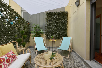 Terrace with fabric and wood hammocks, wicker furniture with fabric seats, decorative plants, stone floors and access door to a living room with aluminum and glass