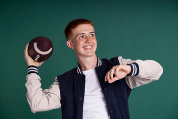 Successful red head boy holding American football ball and looking at camera