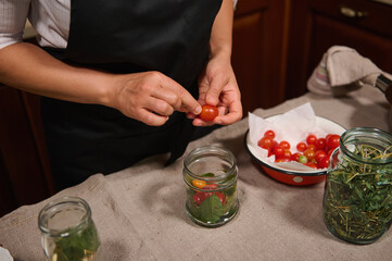 Cropped view of chef's hands putting fresh organic home grown cherry tomato in sterilized jar, while canning delicacy for organic seasonal vegetables for winter. Preserving food. Pickling. Marinating.