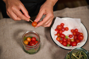 Overhead view of chef's hands putting fresh organic home grown cherry tomato in sterilized jar, while canning delicacy for organic seasonal vegetables for winter. Preserving food. Pickling. Marinating