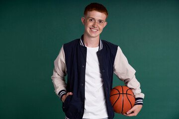 Caucasian red head boy holding basketball ball and looking at camera.