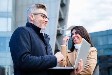 Obraz premium Business people smiling and bringing new business ideas in to life - Two workers standing and discussion about work outside office. Concept of teamwork and workgroup