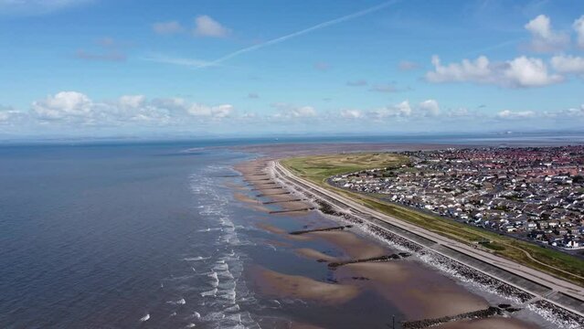 Aerial view of waves crashing onto the coast with views of buildings and houses in the distance. Taken in Cleveleys Lancashire England. 