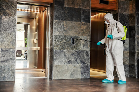 By disinfecting the space and air against the symptoms of coronavirus - fever, cough, headache. A man in a protective uniform cleans high-risk areas of infection such as elevator buttons