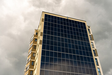 A modern energy-efficient building against the background of clouds. Multi-storey residential building with solar panels on the wall. Renewable energy sources in the city
