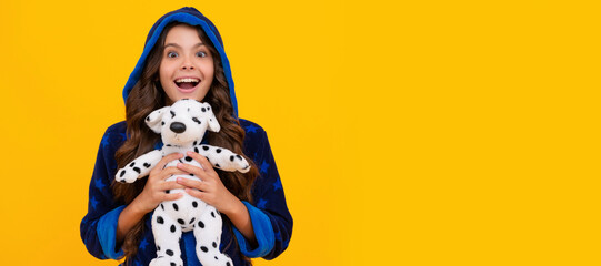 Excited kid happy smiling in hooded bathrobe holding plush toy yellow background, childhood. Banner of child girl with toy, studio portrait, header with copy space.