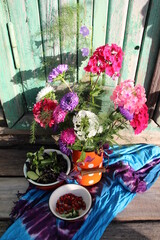 Rustic still life with garden flowers in can, aronia berries and strawberry in bowl on textile cover on old wooden background in sun light