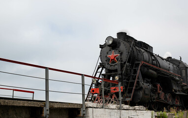 a large black vintage steam locomotive with a red star on the front drives onto a small bridge...