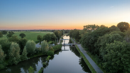 Fototapeta premium Colorful and dramatic sunset over the canal Dessel Schoten aerial photo shot by a drone in Rijkevorsel, kempen, Belgium, showing the waterway in the natural green agricultural landscape. High quality
